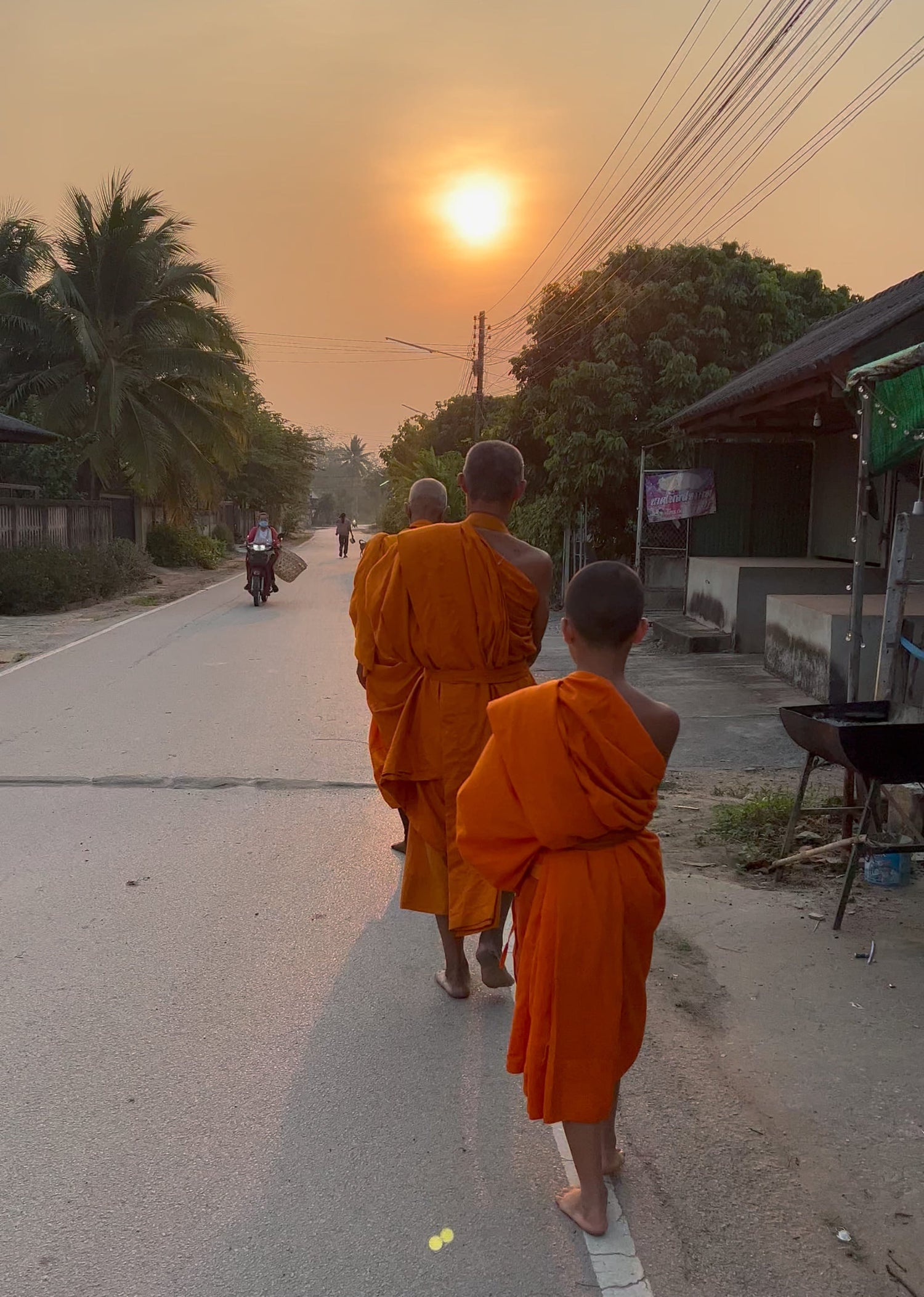 Drei buddhistische Mönche in safranfarbenen Roben beim morgendlichen Almosengang in Chiang Mai bei Sonnenaufgang – ein authentischer Moment thailändischer Kultur, der Oversea Crate inspiriert.